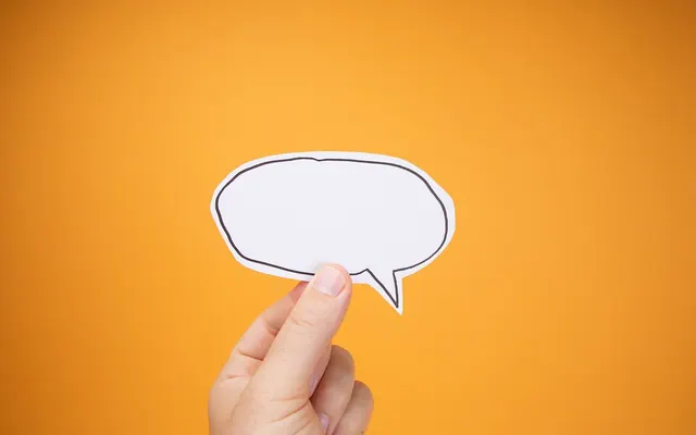 Human Hand Raises Paper Speech Bubble Against Orange Backdrop (53182722835)